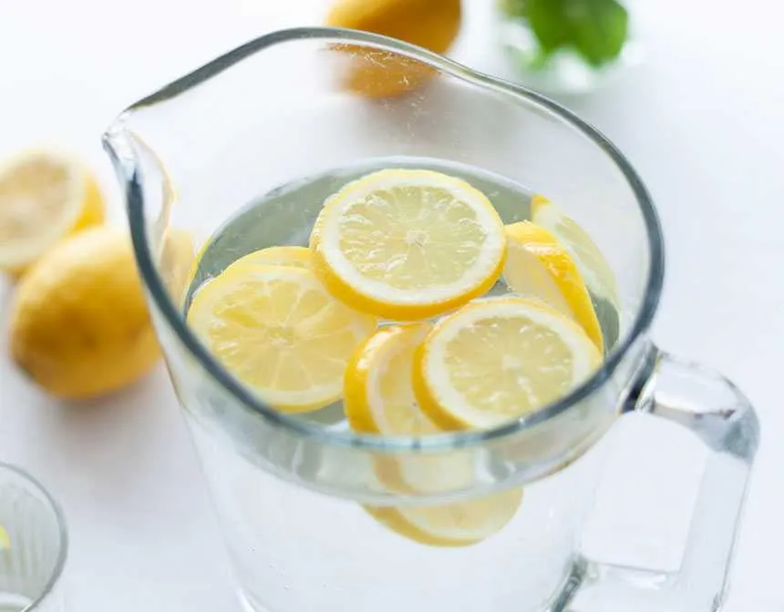 Clear glass pitcher filled with lemonade and slices of lemon