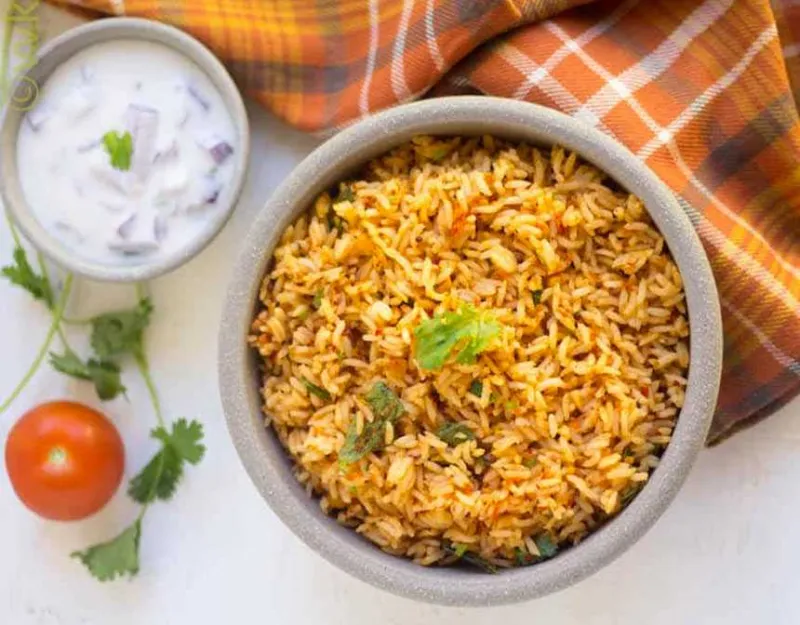 Tomato rice next to a tomato