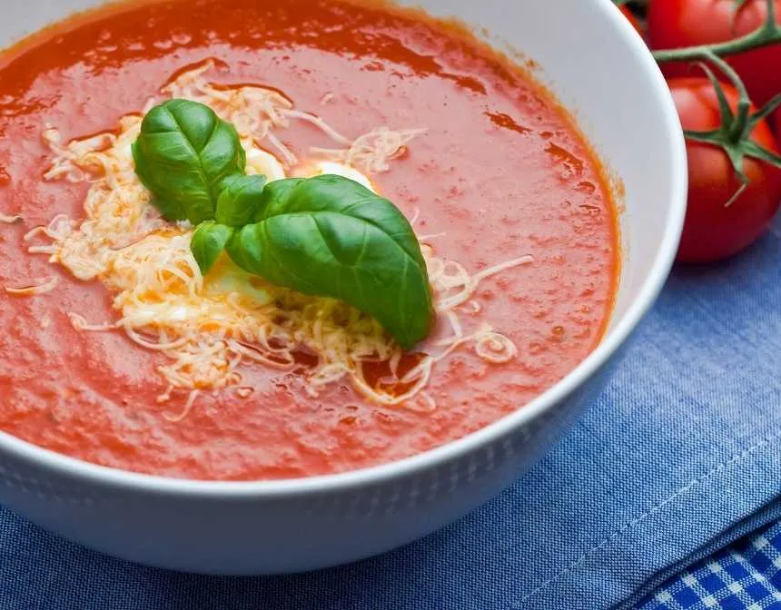 Tomato soup with basil and shredded cheese near tomatoes