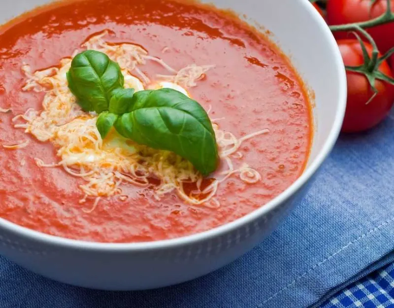 Tomato soup with basil and shredded cheese near tomatoes